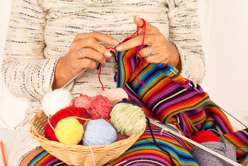 女人用篮子里的线缝编织一条彩色围巾