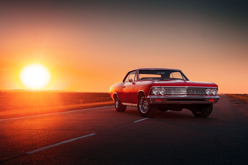 日落时分站在柏油路上的复古红色汽车
