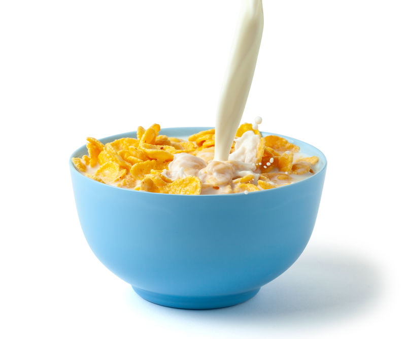 玉米片加牛奶的干早餐一股带奶酪的牛奶和溅洒在蓝色盘子里的谷类食品白底隔离