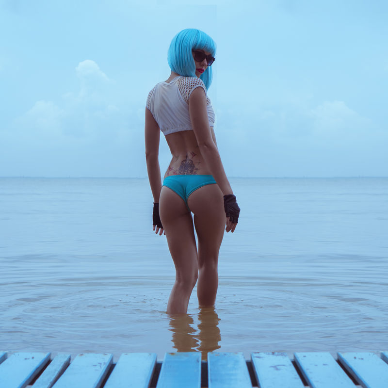 性感美女的背影在现代未来风格中装扮成大海女性穿着比基尼蓝色假发黑色皮革无指手套在水中的创意表情