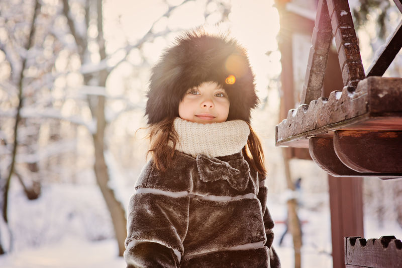 在冬日森林里散步时戴着皮帽和皮衣的快乐可爱的小女孩在喂鸟人附近
