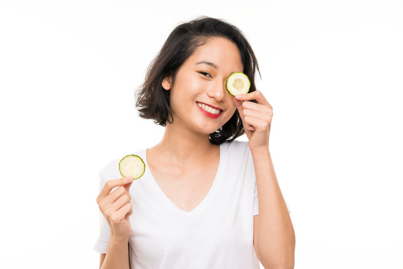 独立背景下的亚洲年轻女子拿着黄瓜片