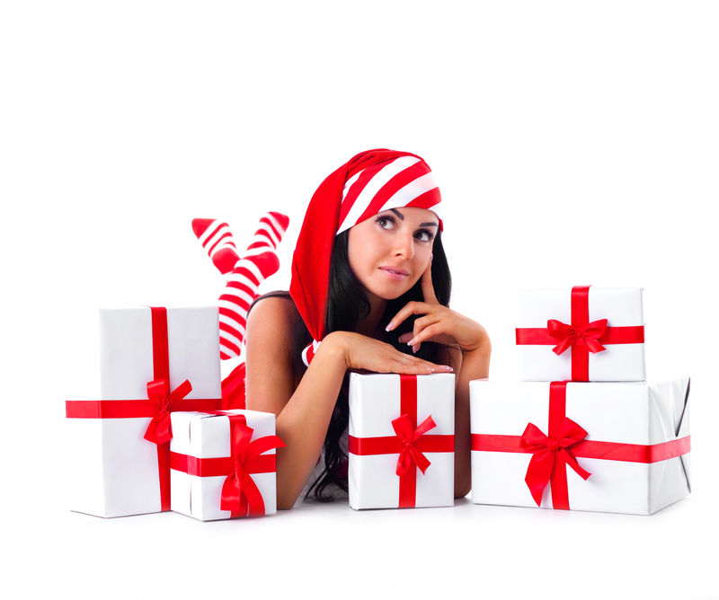 漂亮的小黑发女人打扮成圣诞老人坐在地板上手里拿着很多礼物