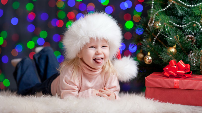 穿着圣诞帽的女婴带着礼物躺在圣诞树旁