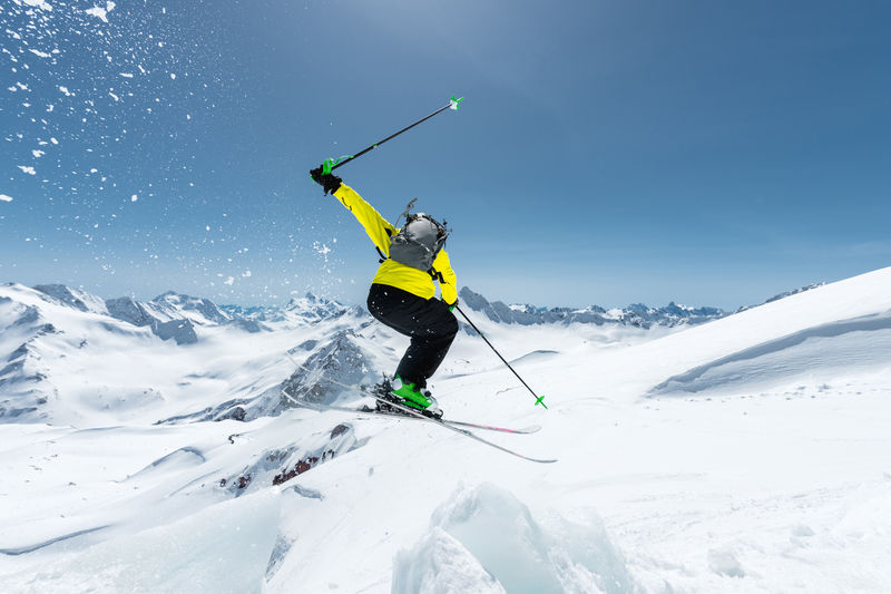 在蓝天和白种人雪山的映衬下-一名身穿全套运动装备的滑雪者从冰川顶部跳入深渊-从后面看-埃尔布鲁斯地区