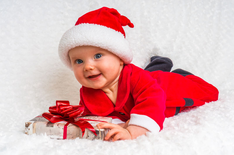 有趣的圣诞女婴躺在白色毯子上带着礼物