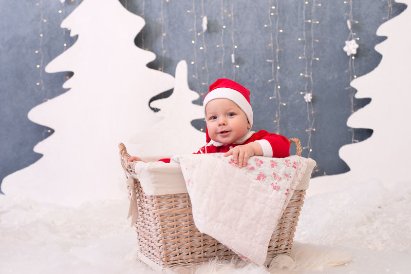 打扮成圣诞老人的孩子坐在白色背景装饰树上的篮子里