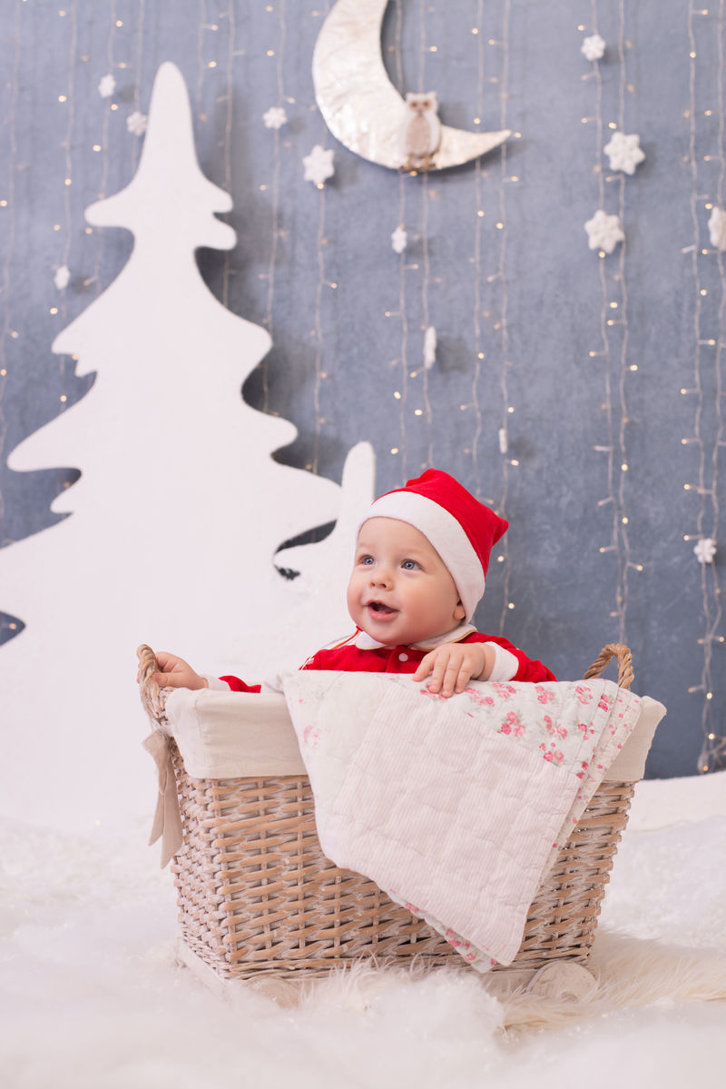 打扮成圣诞老人的孩子坐在白色背景装饰树上的篮子里