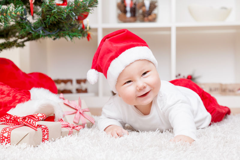 圣诞树旁戴圣诞帽的可爱婴儿带礼物