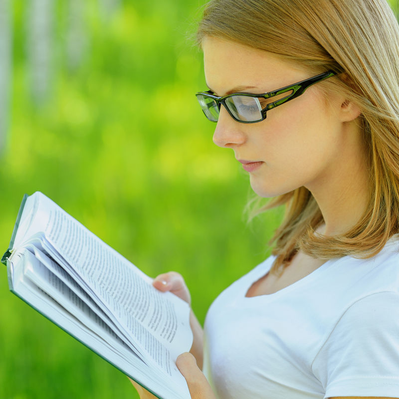 一幅年轻迷人的金发女人拿着书-穿着白衣服-戴着眼镜-站在夏绿园的画像