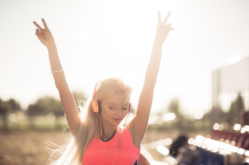 穿着运动服的年轻女子喜欢并微笑着用橙色耳机听音乐她举起双手享受生活