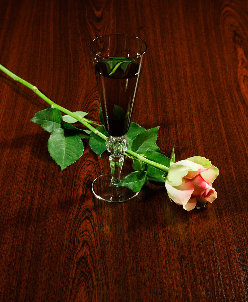 优雅的酒杯和深色木背上精致的花玫瑰