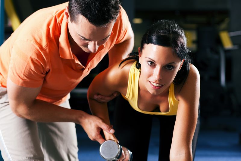 带着私人健身教练在健身房用哑铃锻炼的女人