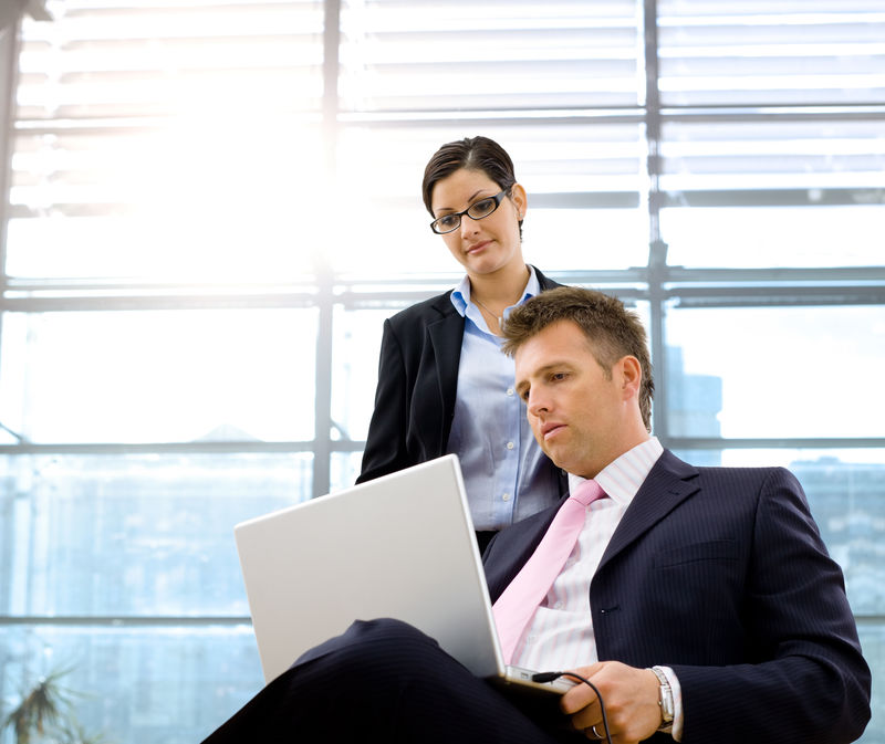 严肃成熟的商人坐着用笔记本电脑-女商人站着一起工作