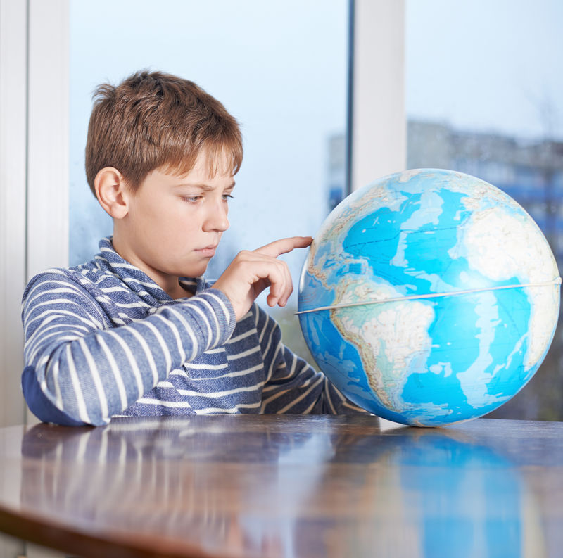 专注的12岁男孩坐在木制的书桌旁-看着地球仪-靠窗构图