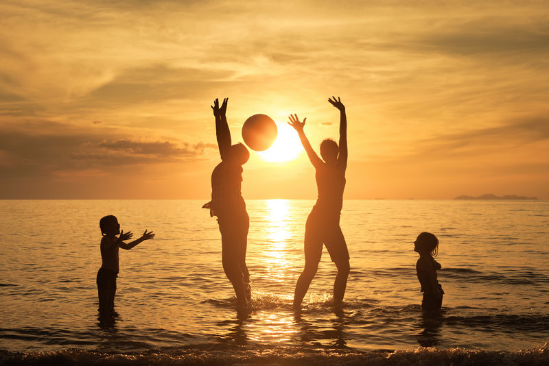 日落时分在海滩上玩耍的快乐家庭的剪影-友好家庭的概念