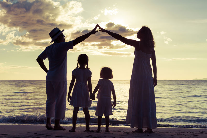 日落时分在海滩上玩耍的快乐家庭的剪影-友好家庭的概念