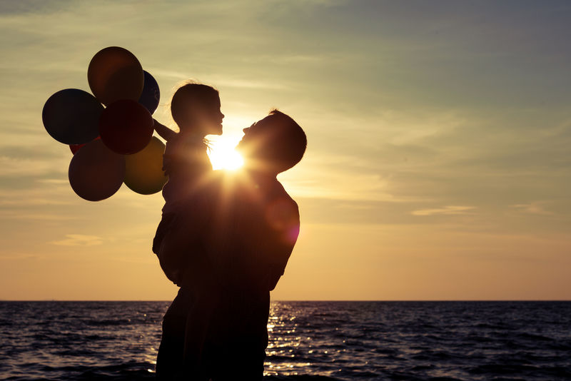 日落时分-爸爸和女儿带着气球在海滩上玩耍-友好家庭的概念