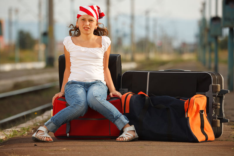 年轻女孩坐在行李上在车站等火车