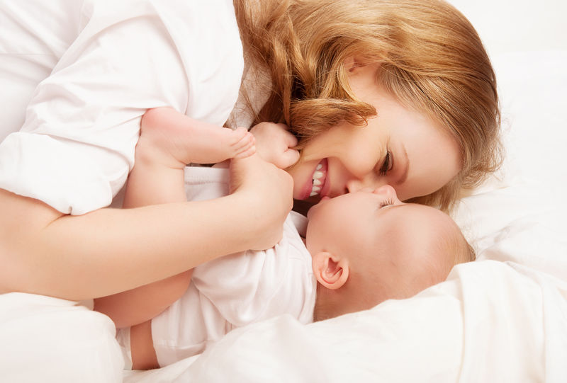 家庭幸福婴儿和母亲玩耍亲吻挠痒痒在床上笑
