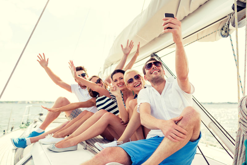 假期-旅行-大海-友谊和人的概念-微笑的朋友坐在游艇甲板和自拍