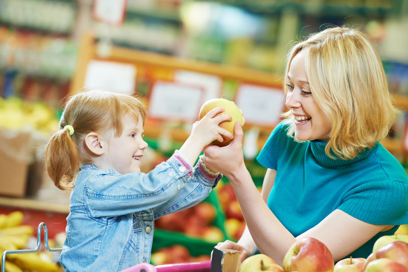 在水果蔬菜超市购物时选择苹果的女人和小女孩