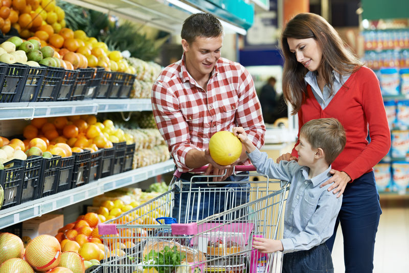 在蔬菜超市购物时带着男人和孩子的女人选择瓜果