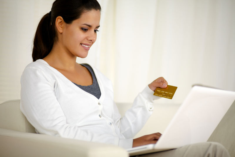 一位迷人的年轻女子在家里用笔记本电脑在网上购物时拿着一张金卡