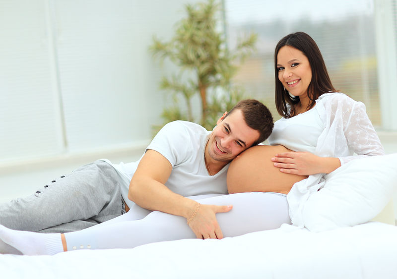 这个男人靠在他怀孕的妻子躺在床上的婴儿包上