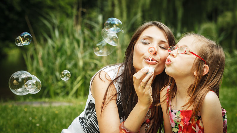 家庭幸福和无忧无虑的概念-妈妈和女儿在公园里玩着吹肥皂泡的游戏-绿色模糊的背景