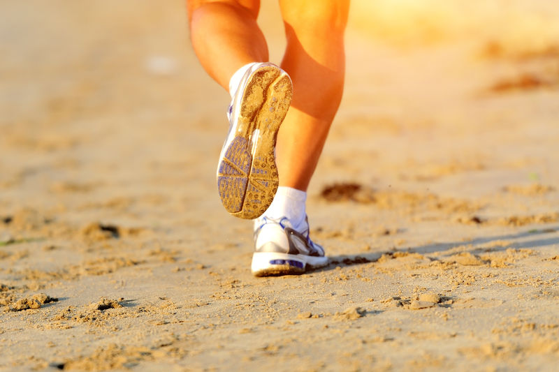 跑步者的脚在沙滩上跑特写镜头在鞋子上
