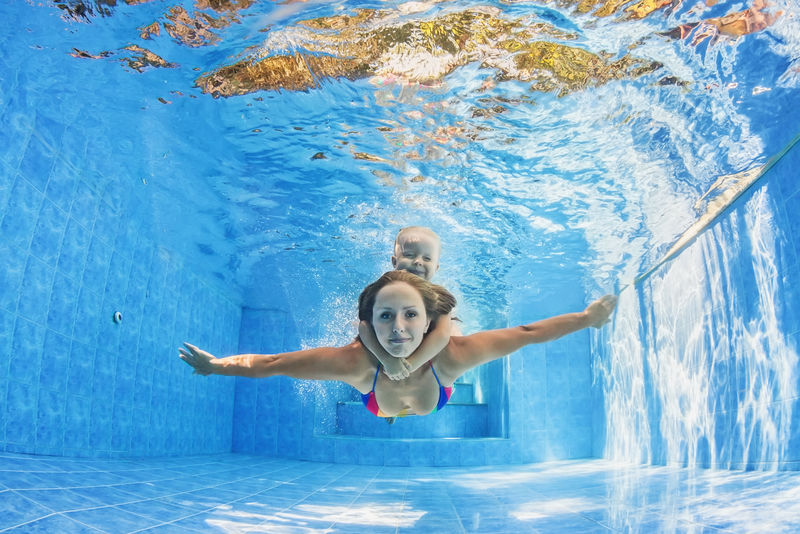快乐的家庭-积极的母亲与女婴游泳和潜水水下乐趣在室外游泳池健康的生活方式积极的家长和有孩子的暑假参加水上运动