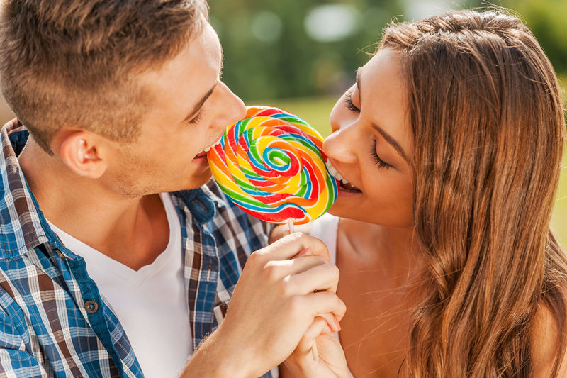 棒棒糖的乐趣-年轻情侣站在户外一起品尝多色棒棒糖