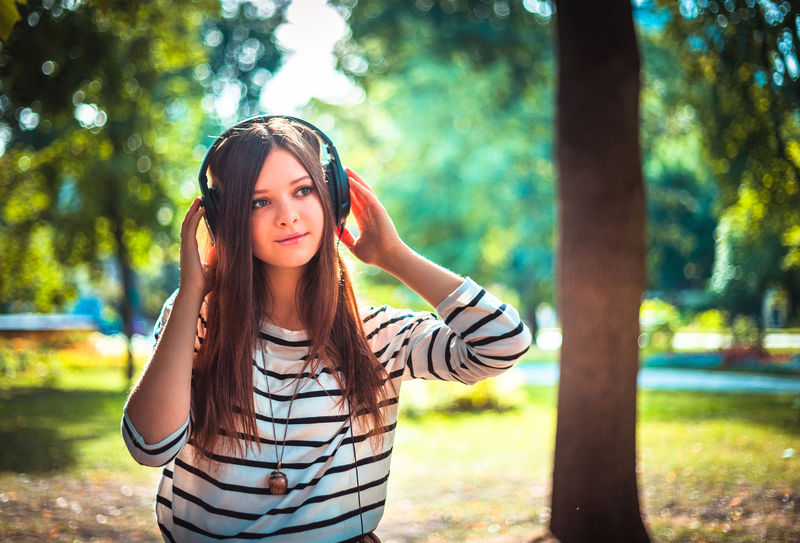 在公园里用耳机听音乐的年轻女孩-高加索人快乐青年学生