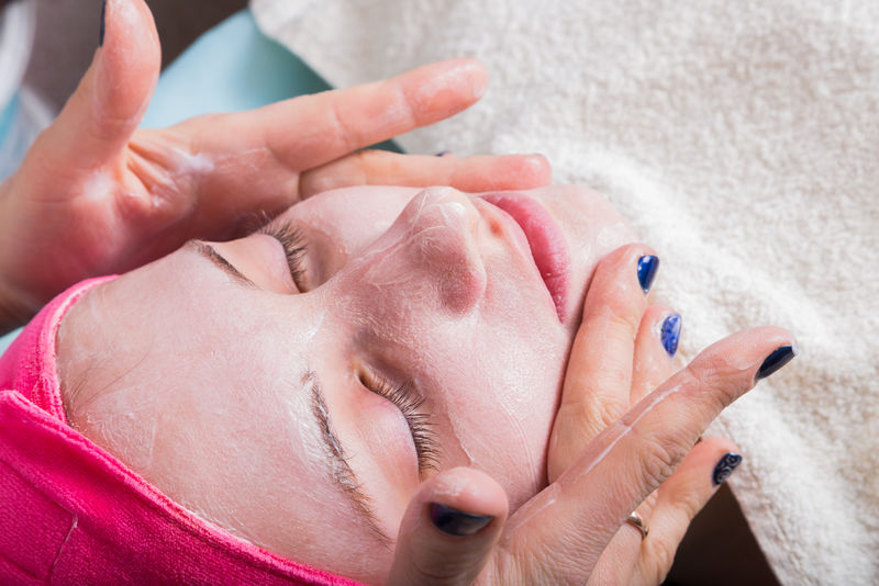 在女孩的脸上涂上焕发活力的面膜-面部整容程序-美容师把面具涂在女孩的脸上-美容院的面部护理
