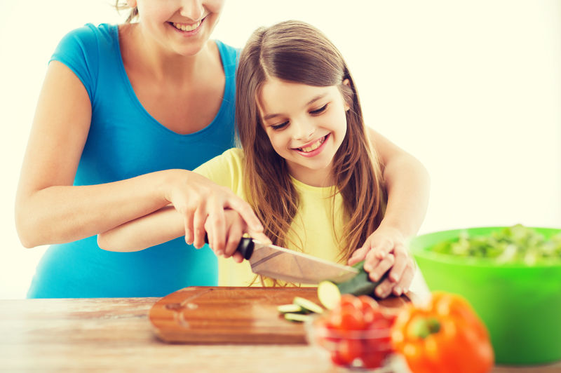 家庭、孩子、烹饪和家庭概念-微笑的小女孩和妈妈在厨房里切黄瓜