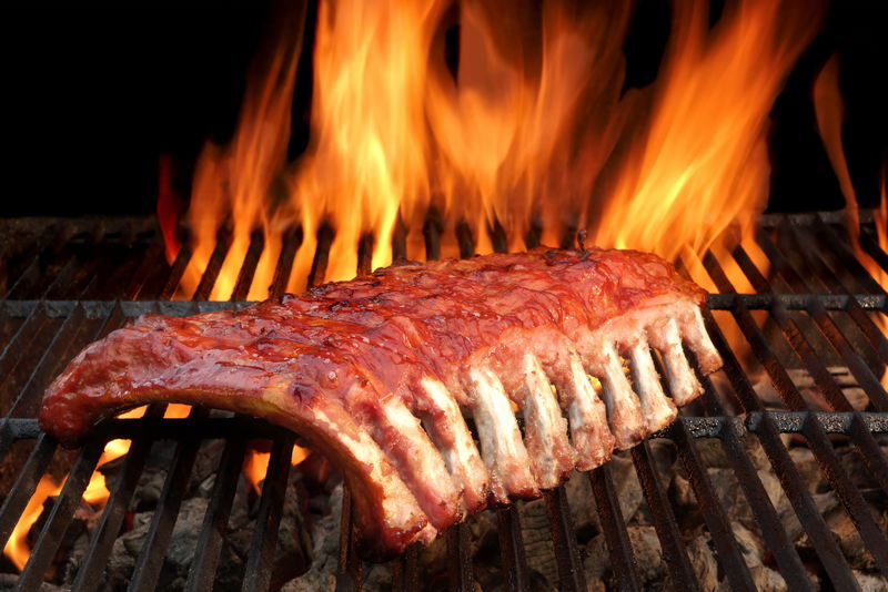烧烤婴儿背部辛辣和熏猪肉排骨在炎热的木炭烤架与明亮的火焰黑色背景-户外聚会或野餐的好零食