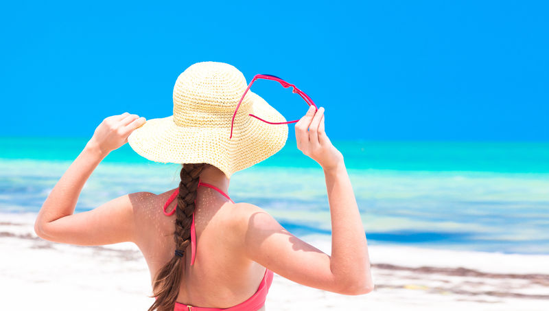 热带海滩上戴草帽和比基尼的女人的后视图