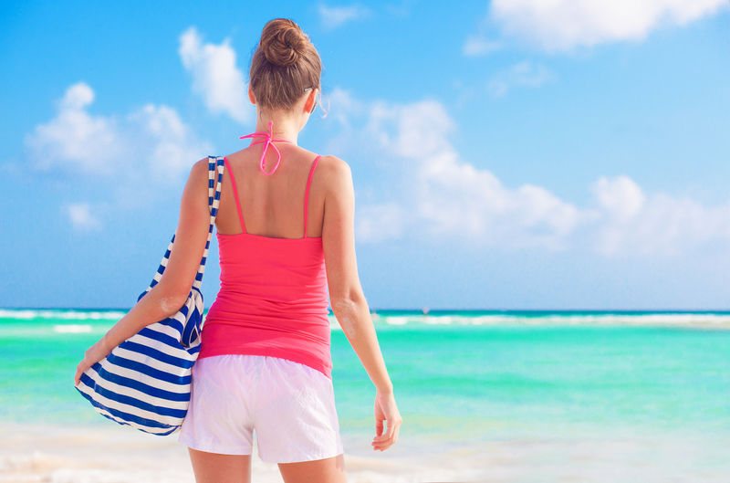 阳光明媚的热带沙滩上，年轻漂亮的女士和沙滩袋的背影
