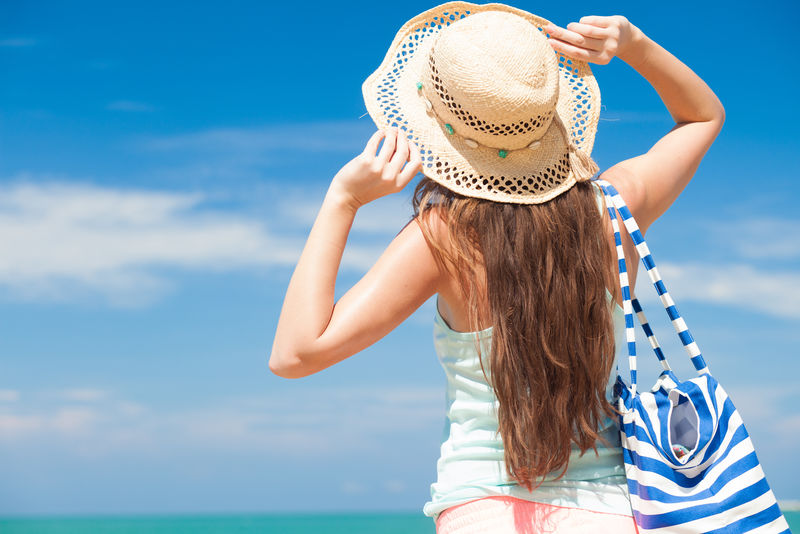 热带海滩上一位穿着条纹包的年轻女性的后视图
