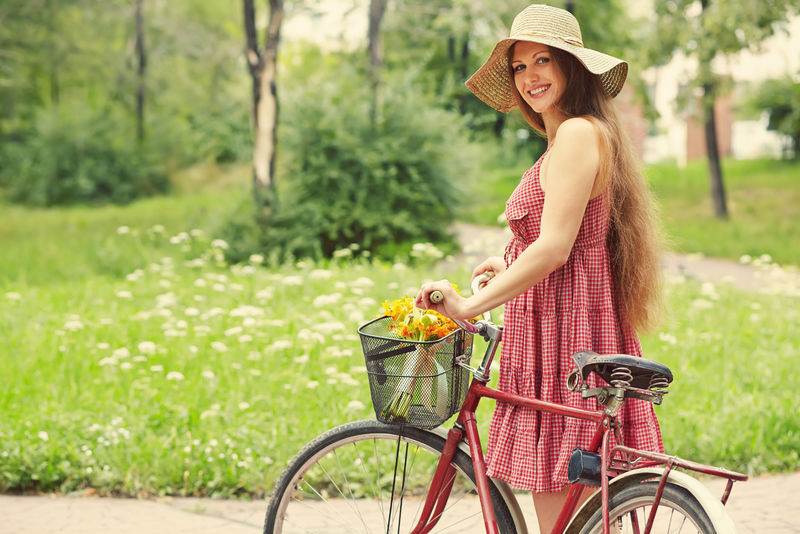 在一个夏日公园里-一个穿着连衣裙戴着帽子骑着自行车的年轻女人-积极的人-户外