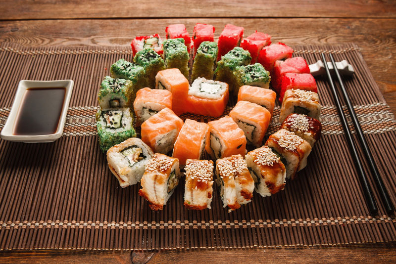 丰富多彩的日本寿司，美食艺术。美味的乌拉马基卷呈彩色螺旋形摆在棕色草席上，特写。东方豪华餐厅菜单照片。