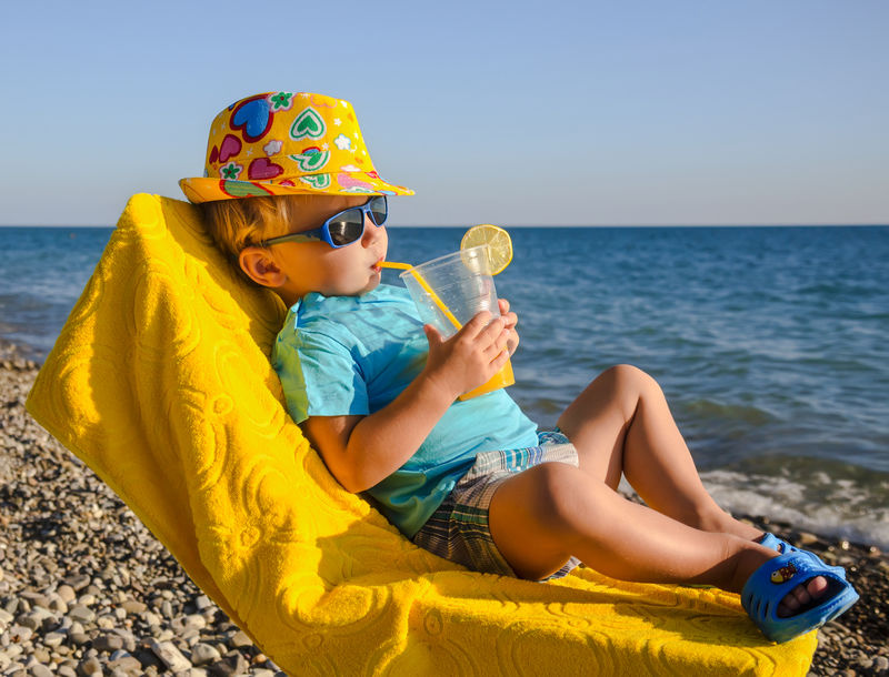 男孩坐在扶手椅上-靠海的海滩上有果汁杯
