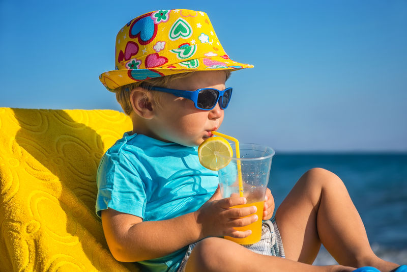 在阳光明媚的日子里-有趣的孩子在海边喝小管里的果汁