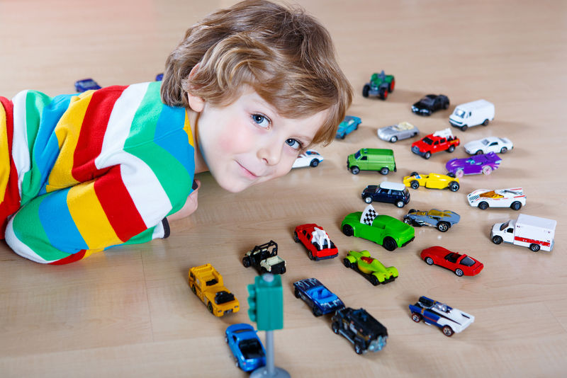 一个金发小男孩在室内玩很多玩具车-孩子穿着彩色衬衫-玩得很开心