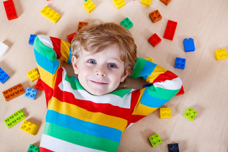 小金发的孩子在室内玩着许多彩色塑料块-男孩穿着彩色衬衫-喜欢建筑和创作