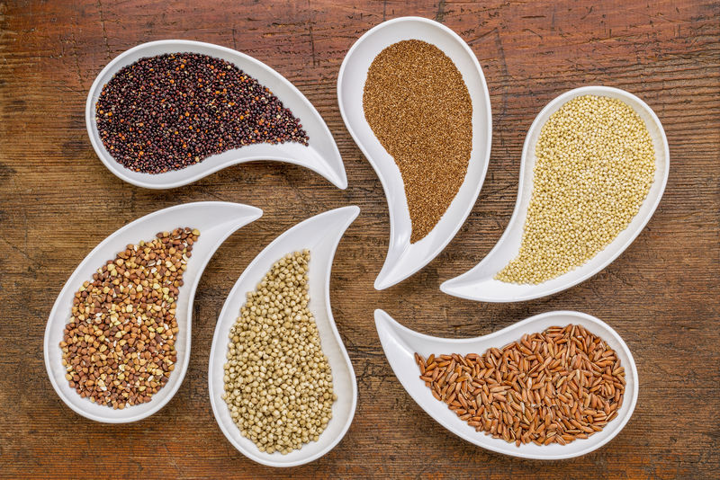 无麸质谷物摘要-含藜麦、teff、小米、大米、高粱和荞麦谷物的泪滴状碗与垃圾木的顶视图