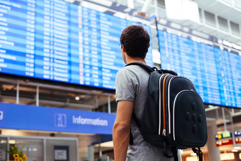 年轻人带着背包在机场附近的航班时刻表