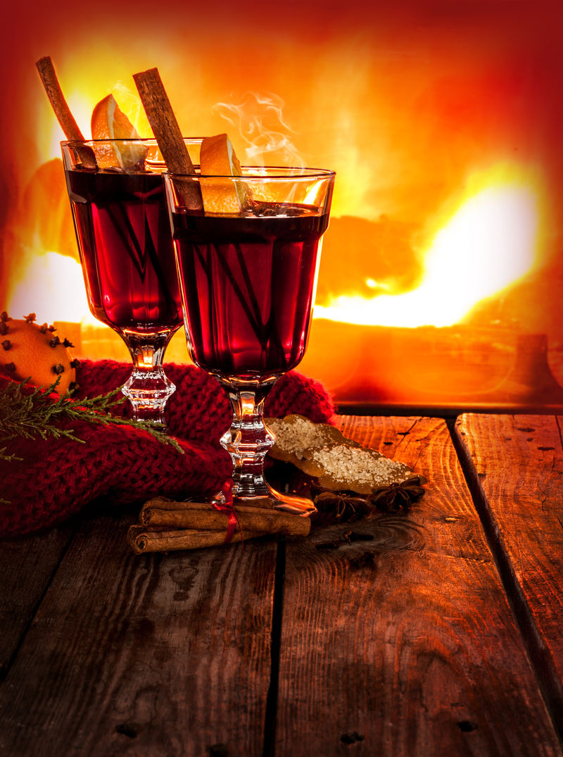 在一杯热的葡萄酒中加入橘子片、茴香和肉桂-放在老式的木桌上-以壁炉为背景-圣诞节或冬季暖饮-具有文本空间的布局