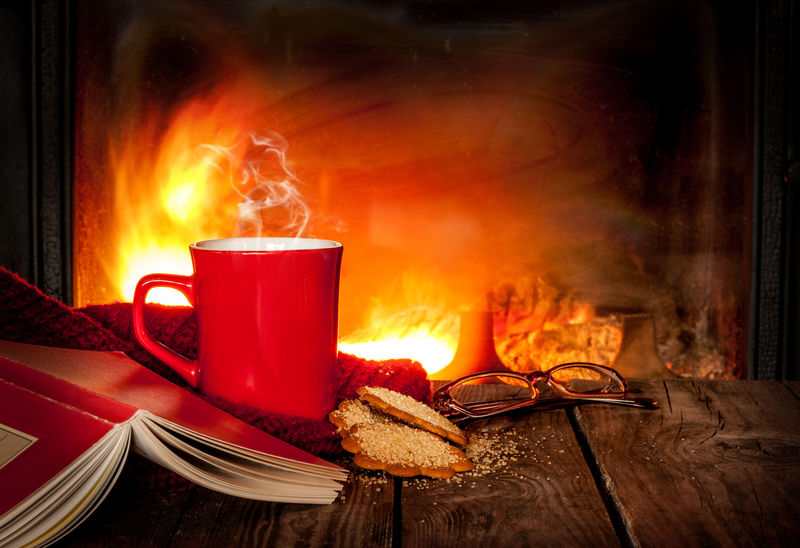 红杯子里的热茶或咖啡-姜曲奇-古旧木桌上的书和玻璃杯-以壁炉为背景-圣诞节或冬季暖饮-具有文本空间的布局